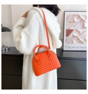 Orange V-quilted faux leather shell bag shown with crossbody strap on a female model
