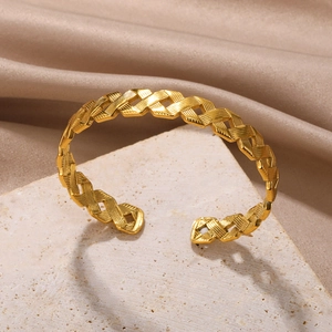 Detail of gold open bangle with woven hollow texture on a white textured stone base