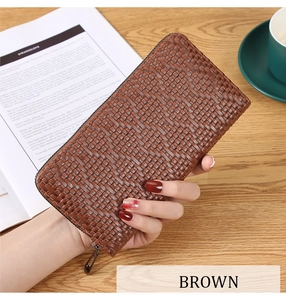 Detail of brown long wallet with woven texture shown on desk with lifestyle accessories