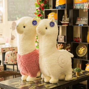 Detail view of two cute alpaca plush toys standing on a table in a cozy indoor setting