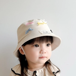 Detail of beige children's sun hat featuring colorful bows and decorative fabric label