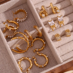 Detailed close-up of 18K gold plated earrings with pearls and crystals on beige velvet