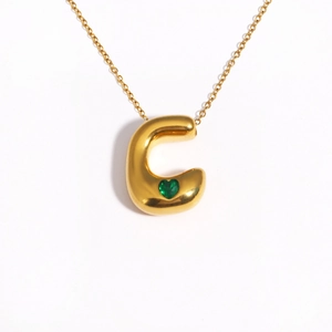 Detail of 18k gold plated bubble letter C pendant with a green heart-shaped gemstone