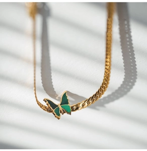 Detail of 18K gold Cuban chain anklet featuring a green enamel butterfly charm