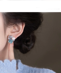 Detail view of pearl and square blue gemstone stud earrings on model's ear