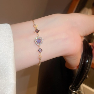 Detail of adjustable gold bracelet featuring a purple zircon sunflower charm with fine crystals