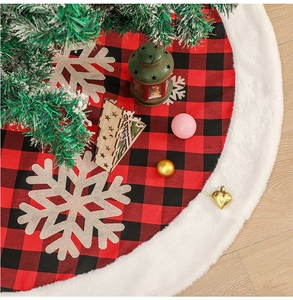 Macro detail of red and black plaid Christmas tree skirt with white plush trim and snowflakes