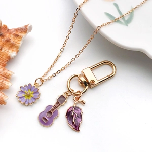 Detail of purple daisy pendant necklace and guitar keychain in polished gold alloy