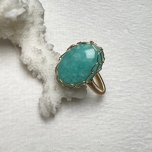 Macro shot of handmade wire-wrapped gold ring with oval turquoise stone on white coral