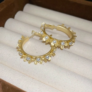 Macro detail of matte gold hoop earrings featuring delicate floral motifs and small pearls