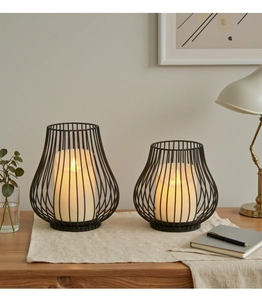Close-up of modern black wire iron candle holders with warm LED lights on a wooden desk