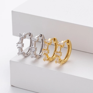 Detailed close-up of gold and silver ear cuffs with rectangular zircon stones on white blocks