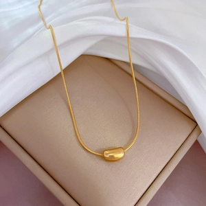 Dettaglio della collana dorata con ciondolo a fagiolo su una scatola per gioielli