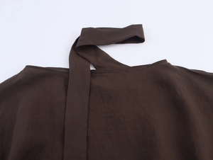 Vue détaillée du haut marron foncé avec col rond et rivets sur la texture du tissu