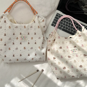 Close-up of pleated seersucker tote bags with animal prints and braided handles on a bed