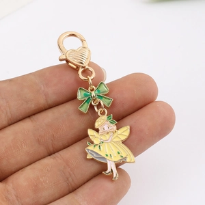 Detail of fairy keychain with yellow dress, green bow and golden heart clasp held in hand