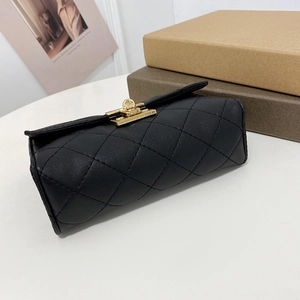 Elegant black quilted cylindrical leather chain bag with a gold twist lock on a desk