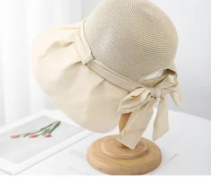 Detail of beige straw sun hat featuring a large fabric bow and flexible adjustment strap