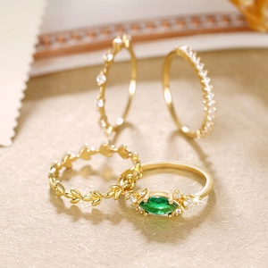Detalle macro del set de 4 anillos dorados con piedra verde esmeralda y hojas grabadas