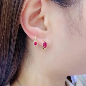 Detail of elegant gold drop earrings with ruby-red stones and white zircon on ear