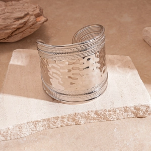 Detailed close-up of wide silver metal cuff bracelet with hammered texture and beaded edges