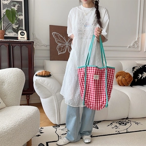 Detail of red and white checkered canvas tote bag with cyan handles held in a home setting