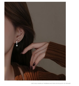 Close-up of minimalist silver star earrings set with zircon stones on a female ear