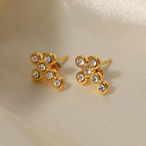 Macro shot of gold-plated cross stud earrings with sparkling crystals on white satin