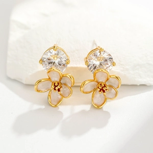 Macro shot of gold-plated floral earrings with white enamel petals and clear zircon centers