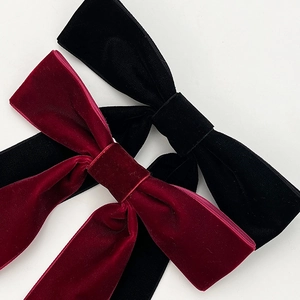 Detail of velvet bow hair clips in wine red and black showing rich fabric texture