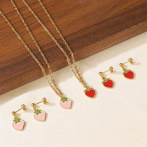 Detail of gold-tone necklaces and stud earrings with red and pink enamel strawberry charms