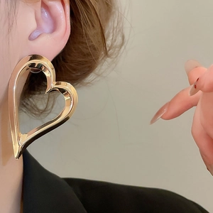 Detailed view of polished large hollow heart-shaped gold earring on model's ear