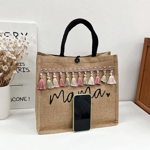Linen tote bag with black Mama print and colorful tassels in a clean lifestyle setting