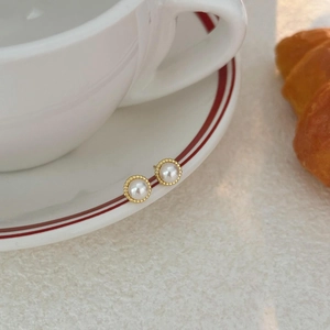 Elegant white pearl stud earrings with gold milgrain trim on a white porcelain tray