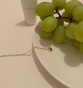 Close-up of a 3D gold heart pendant necklace on a minimalist white tray with fresh grapes