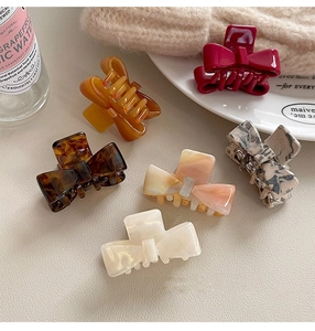 Flat lay of multiple acetate bow hair claws in various marble and solid colors on leather