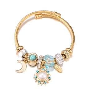 Detail of gold DIY charm bracelet with blue gemstone, pearl and handmade engraving