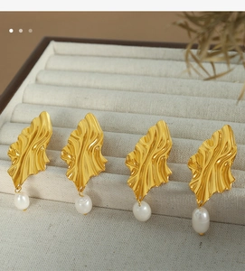Detailed view of elegant gold leaf earrings with white pearls on a velvet jewelry stand