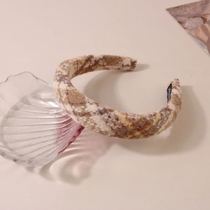 Detailed texture of plaid wool headband with beige and brown patterns and handmade label