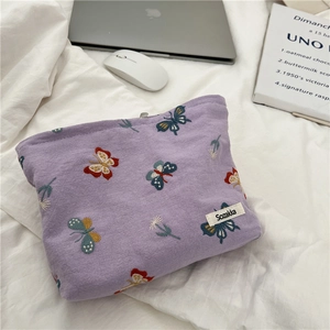 Detailed embroidery of colorful butterflies and flowers on purple fabric pouch with logo