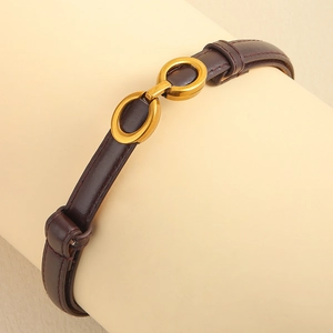 Détail d'une ceinture fine en cuir marron foncé avec boucle ovale dorée entrelacée