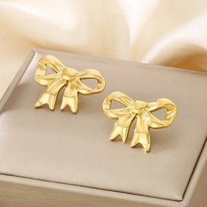 Close-up of golden hollow bow earrings on a beige velvet jewelry box background