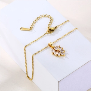 Gold stainless steel leaf pendant necklace with marquise zircons on white pedestal