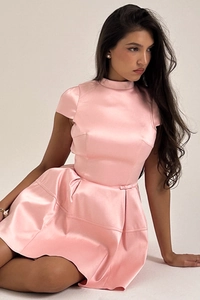 Dettaglio del tessuto in raso rosa di un abito corto con collo alto e gonna a pieghe