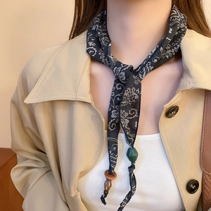 Detail of vintage paisley silk scarf necklace with green and wood beads on beige coat