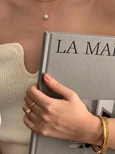 Close-up of a gold woven texture bangle paired with elegant pearl jewelry on a model