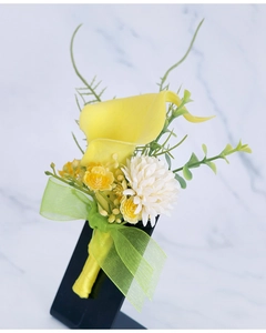 Detail of yellow calla lily boutonniere with white flowers and ribbon for groom and wedding