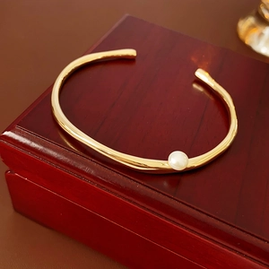 Detail of a minimalist gold geometric open bracelet with a white pearl on a wood gift box