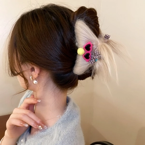Detail of a beige plush monster hair claw clip with heart sunglasses on a model's hair