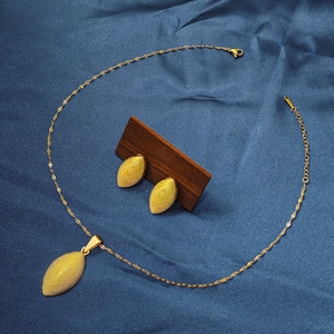 Golden textured oval leaf necklace and earring set displayed on elegant blue silk fabric